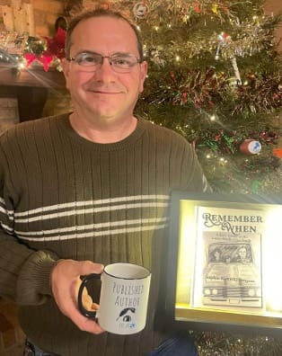 Argyle Fox Publishing author Stephen McKinley Simpson holds his first book, Remember When, and holds a coffee mug that reads "Published Author," while standing in front of a Christmas tree.